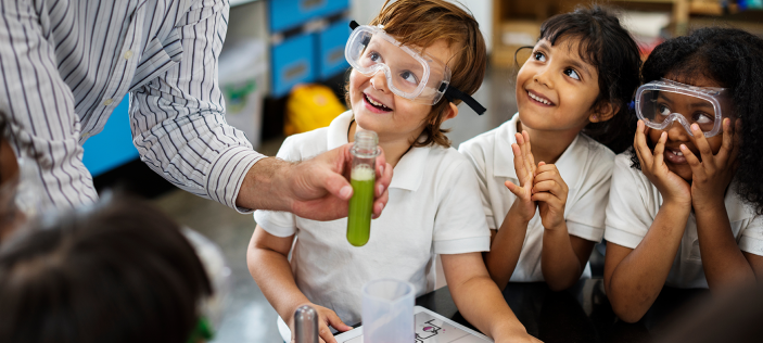 Happy school children wearing safety goggles and looking at teacher