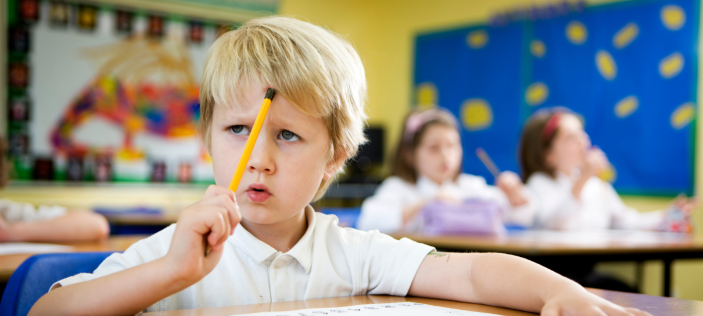 Confused looking school-child holding pencil to forehead