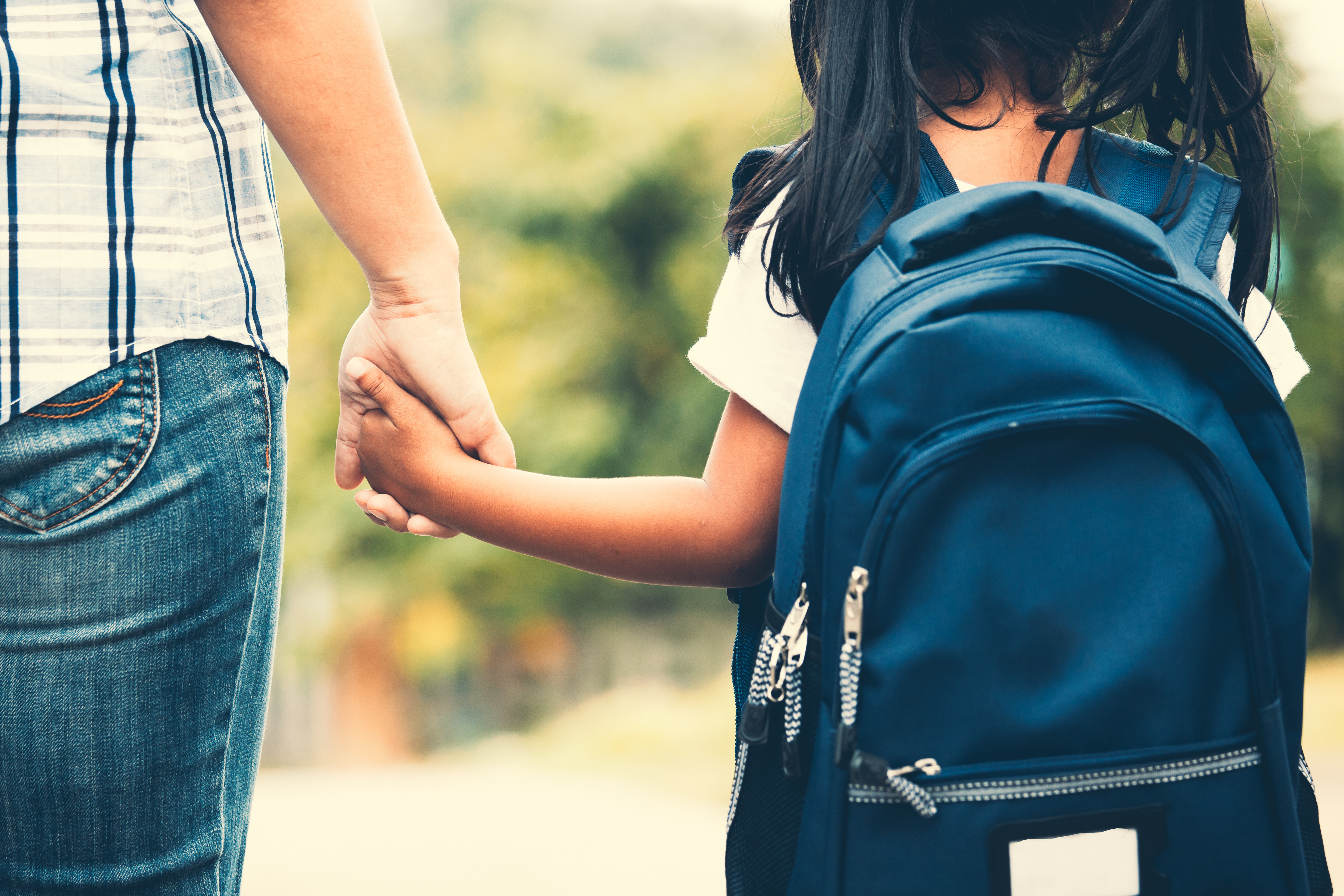 Child wearing blue pack pack holding an adults hand