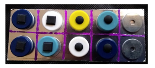 Picture 9 description: A tactile tens frame made with cardstock, puff paint to represent the frame, metal washers and magnets with round and square bumpons to represent two different amounts.