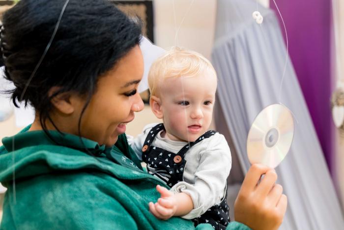 Young person holding a toddler in one hand and showing the toddler a CD with her other hand