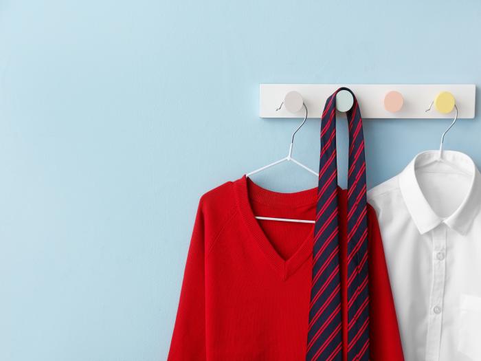 Stylish school uniform hanging on colour wall