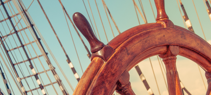 Wooden wheel of a sailing ship in a blue sky with rigging in background