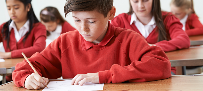 Class in red jumpers writing in exercise books