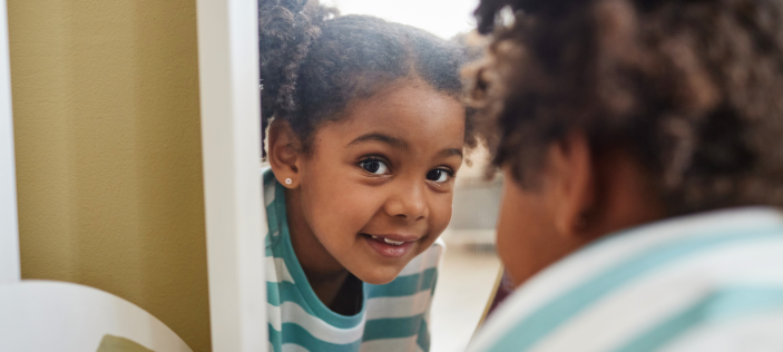 Young child looking back at us through her reflection in a mirror 