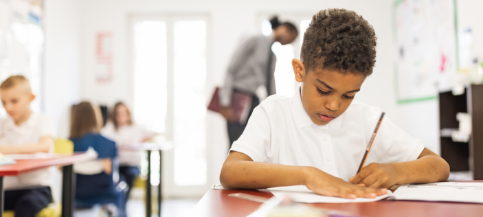 Child writing at desk with pencil 