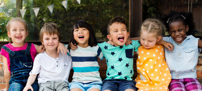 Happy Early Years children sat together with arms round eachother