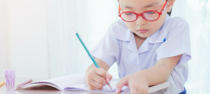 Child with red glasses writing in book