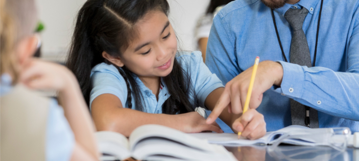 primary girl writing with a teacher