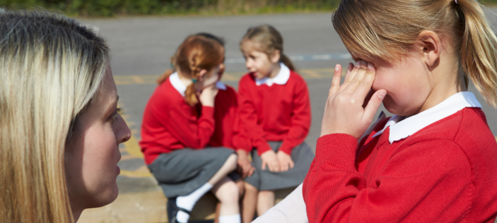 Adult talking to a girl in a red uniform with two others in the background
