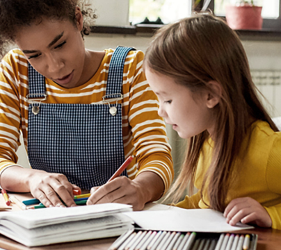 Woman wearing yellow writing in book with a girl wearing yellow