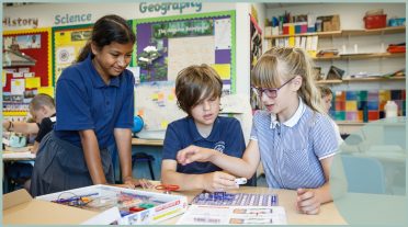 girl standing up with boy and girl sitting in classroom
