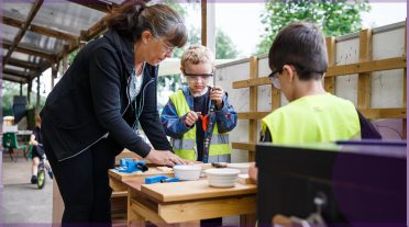 lady helping 2 children outdoors wearing safety equipment