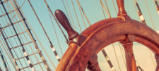 Wooden wheel of a sailing ship in a blue sky with rigging in background