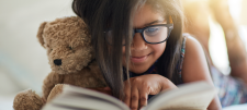 Girl reading book with teddy