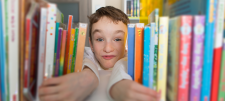 Child peeking through books on a shelf