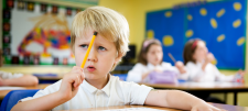 Confused looking school-child holding pencil to forehead