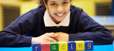 School girl in blue top smiling next to coloured word blocks which spell out "reading"