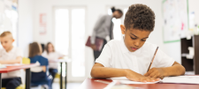 Child writing at desk with pencil 