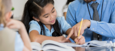 primary girl writing with a teacher