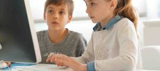 Two children looking at a computer monitor 
