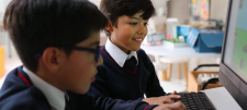 Two children in uniform looking at a computer monitor