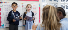 Boy and girl reading out of a book as other children look on