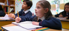 Girl in blue uniform sat at desk with yellow pencil in her hand